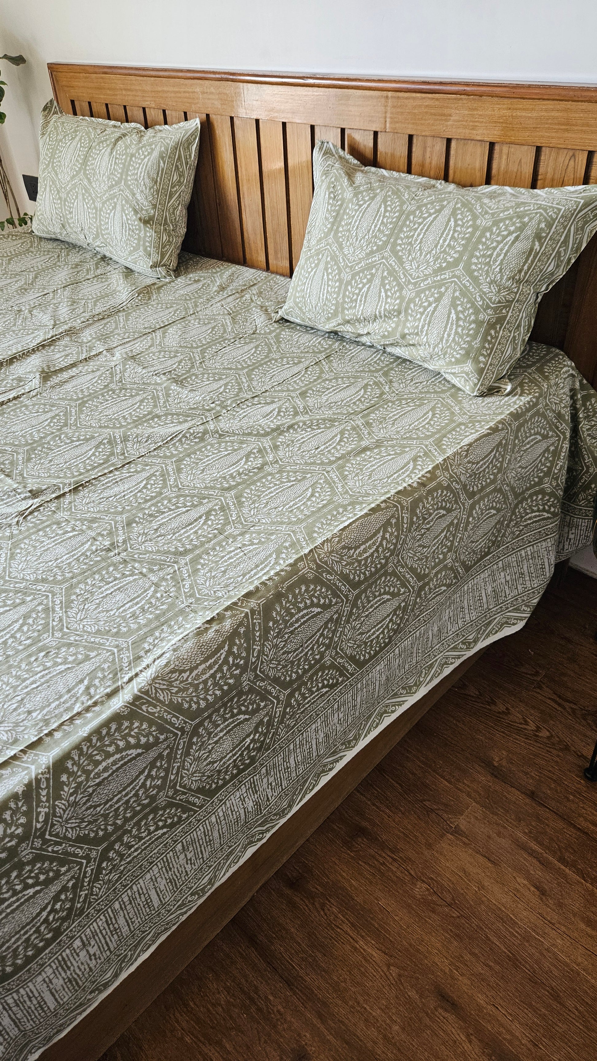 Green patterned quilt and pillows on a wooden bed frame.